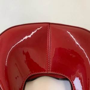 Detail view of the red patent leather handbag showing stitching and black zipper texture