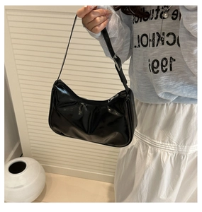 Detail of black patent leather crescent bag with glossy finish and silver metal zipper