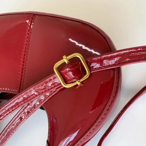 Close-up of red patent leather handbag featuring glossy texture and golden metal buckle