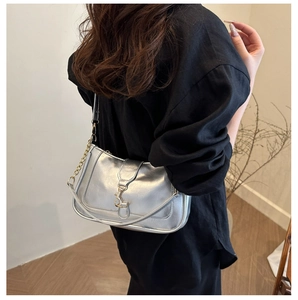 Détail du sac à bandoulière argenté métallisé avec chaîne dorée sur chemise noire