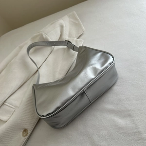 Detail of silver crescent shoulder bag with metallic wrinkled texture on white fabric