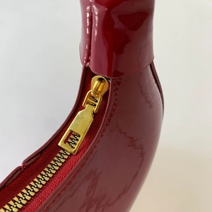 Macro shot of glossy red patent leather handbag featuring premium gold metal zipper details
