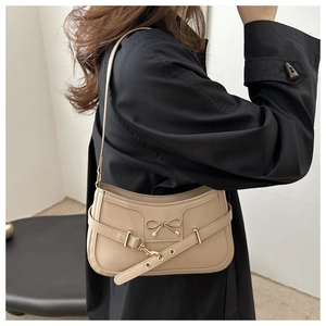 Detail of beige PU leather underarm bag featuring a gold metal bow and eyelet strap