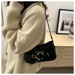Close-up of black underarm bag featuring a metallic bow and gold hardware details