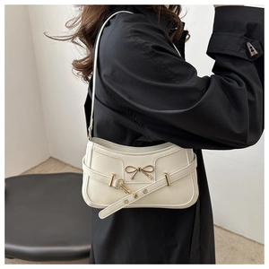 Detail of cream white faux leather bag with golden bow hardware and eyelet strap buckle