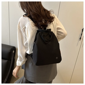Close-up of black nylon backpack with circular metal logo and adjustable shoulder straps