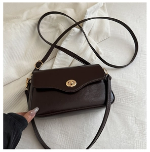 Detail of dark brown patent leather shoulder bag featuring a gold ring twist lock