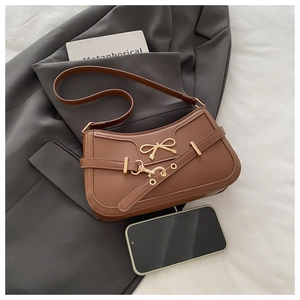 Close-up of caramel brown leather shoulder bag with gold metal bow and eyelet strap