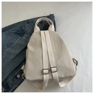 Detailed view of cream nylon bag with fabric straps and top handle on denim background