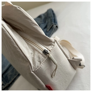 Close-up of beige fabric shoulder bag showing zipper detail and textured nylon material
