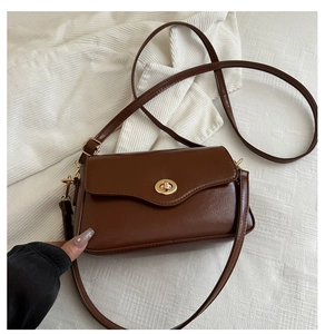 Detail of a brown faux leather crossbody bag with a round gold buckle on white knit fabric
