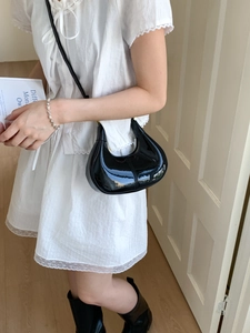 Chic black glossy patent leather crescent shoulder bag styled with an elegant lace dress