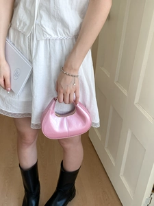 Pink metallic half-moon handbag shown in a fashion lifestyle setting with a white dress