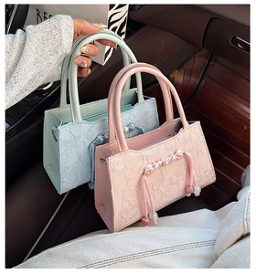Detailed view of lace textured handbags in pink and blue with pearl tassels and ring handles