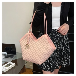 Close-up of pink tote bag with M-pattern print and metal pendant in office setting