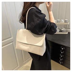 Detail shot of a minimalist cream shoulder bag worn by a model in a modern room