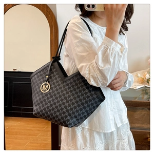 Detail of black tote bag with gray M-letter print and metallic M-pendant charm