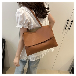 Dettaglio di una borsa a spalla in pelle marrone con texture opaca e patta minimalista