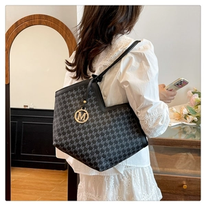 Detail of a large monogram tote bag with golden M pendant shown on model in home setting