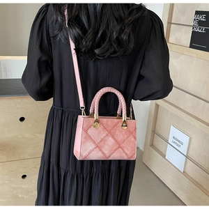 Back view of pink crossbody bag with woven handle on model wearing black pleated dress