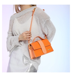 Detail of orange embossed leather handbag with gold metal logo and adjustable strap