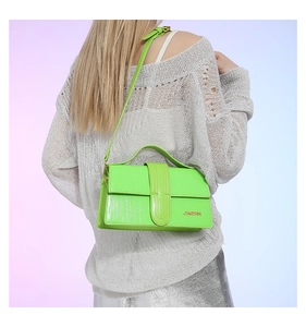 Detail view of a neon green crocodile texture crossbody bag worn by a model in a grey knit