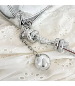 Detail der silbernen Knautschtasche mit geknotetem Gurt und poliertem Metallkugel-Anhänger