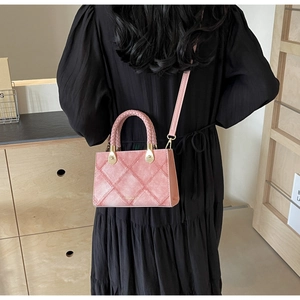Detail of pink quilted crossbody bag with woven handle and gold hardware on model