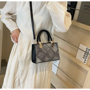 Detail of grey quilted handbag with black braided handle and golden metallic hardware