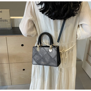 Detail of grey quilted handbag with black woven handle and fashion logo on leather