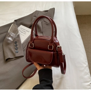 Close-up of a burgundy patent leather shell bag with silver hardware on bedding