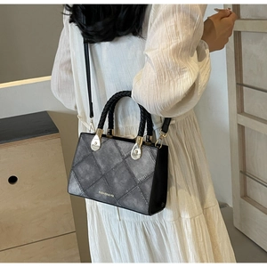 Detail of greyish-black crossbody bag with quilted pattern and golden metal accents
