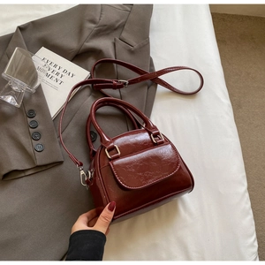 Detail of burgundy shell bag with pleated texture, silver hardware and front pocket