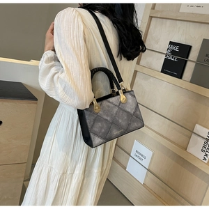 Detail of grey diamond quilted bag with woven handle and gold hardware shown in lifestyle scene