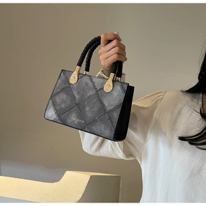 Close-up of gray quilted denim handbag with black braided handles and gold hardware