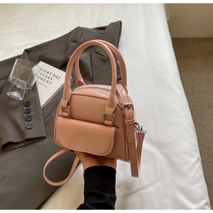 Detail of light pink mini satchel with top handles and silver zipper on white bedding