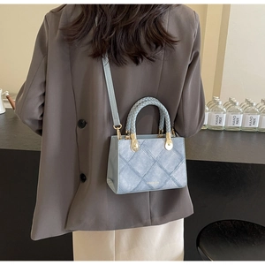 Detail of light blue crossbody bag with quilted pattern, woven handles and gold metal accents
