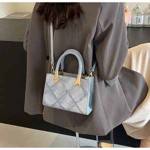 Detail of light blue denim crossbody bag with gold hardware and woven handle on model