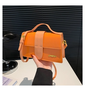 Detailed view of bright orange crocodile embossed leather with gold JINGPIN metal logo
