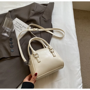 Detail of a creamy white mini shell bag made of cracked PU leather on white bedding