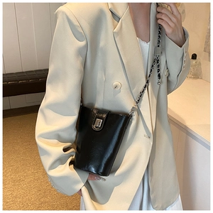 Borsa a secchiello nera lucida con catena d'argento indossata su un blazer beige in dettaglio