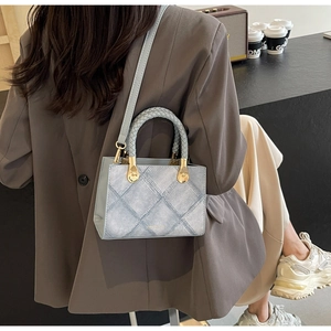 Detail of light blue crossbody bag with denim texture and woven handle on a model