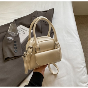 Detail of cream mini shell bag with smooth leather texture and decorative front pocket