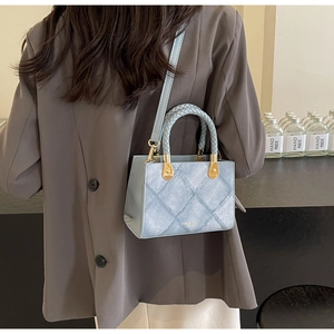 Detail of light blue textured crossbody bag with woven handle and gold hardware detail