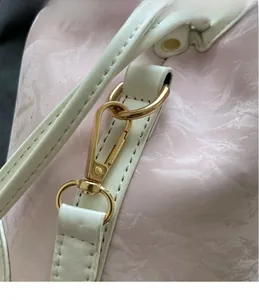 Detailaufnahme der goldenen Metallbeschläge und Nähte an einer rosa Kunstleder-Beuteltasche