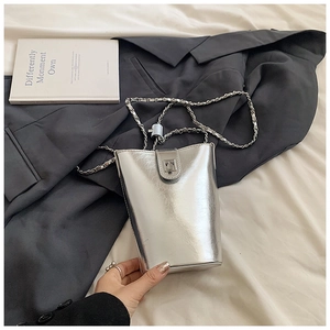 Détail du sac seau métallisé argenté avec bandoulière chaîne sur fond de costume gris