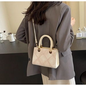 Close-up of beige quilted crossbody bag with woven handle on grey blazer model