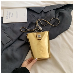 Détail d'un sac seau doré avec bandoulière chaîne sur un blazer gris foncé chic
