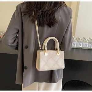 Detail of cream quilted leather handbag with woven handles and gold hardware worn on model