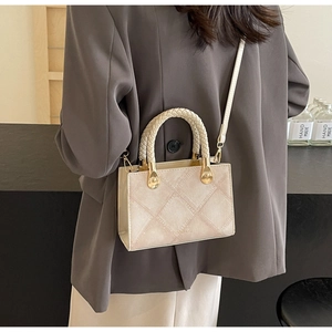 Detail of light beige quilted crossbody bag with woven handle on a grey blazer model